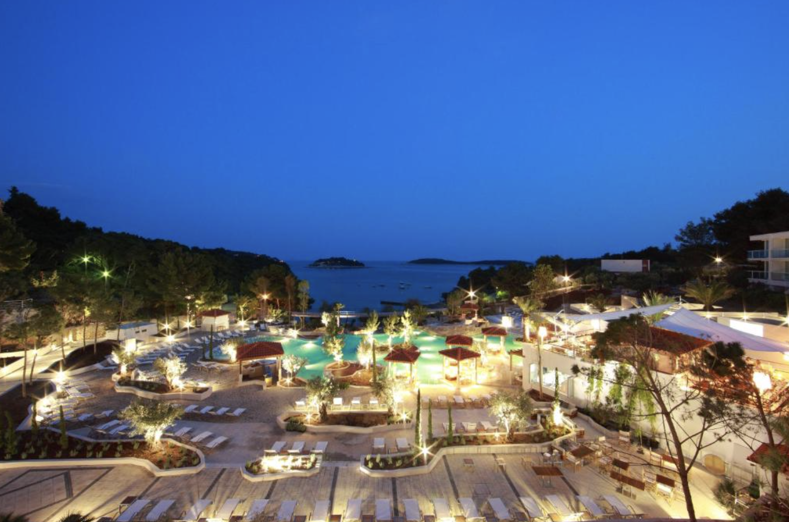 The resort pool terrace lit up at dusk with the bay behind